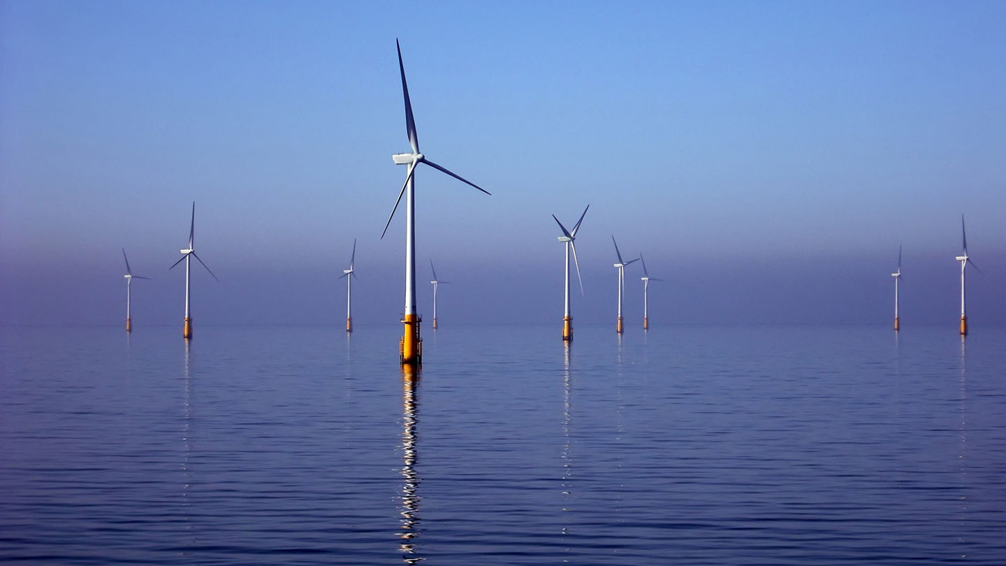 View of ocean and blue sky with several offshore wind turbines.